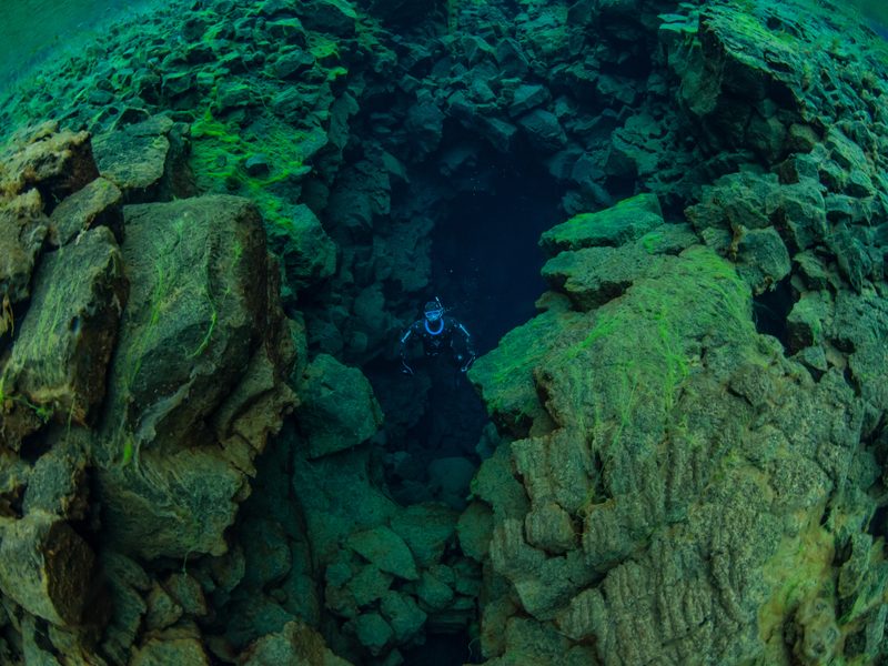 A freediver approaching a narrow moss-covered rock passage in Silfra