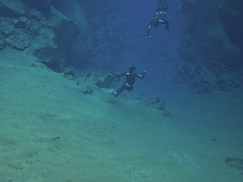 Freedivers gliding along the sandy floor of the Silfra fissure