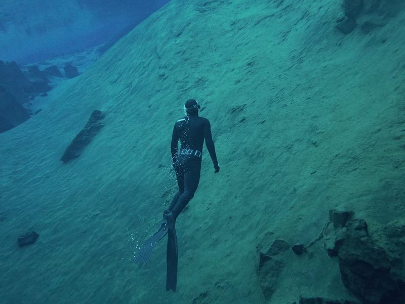 A freediver swimming over the sloped rock floor of Silfra