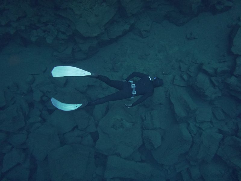 A freediver gliding above rocky terrain on the floor of Silfra
