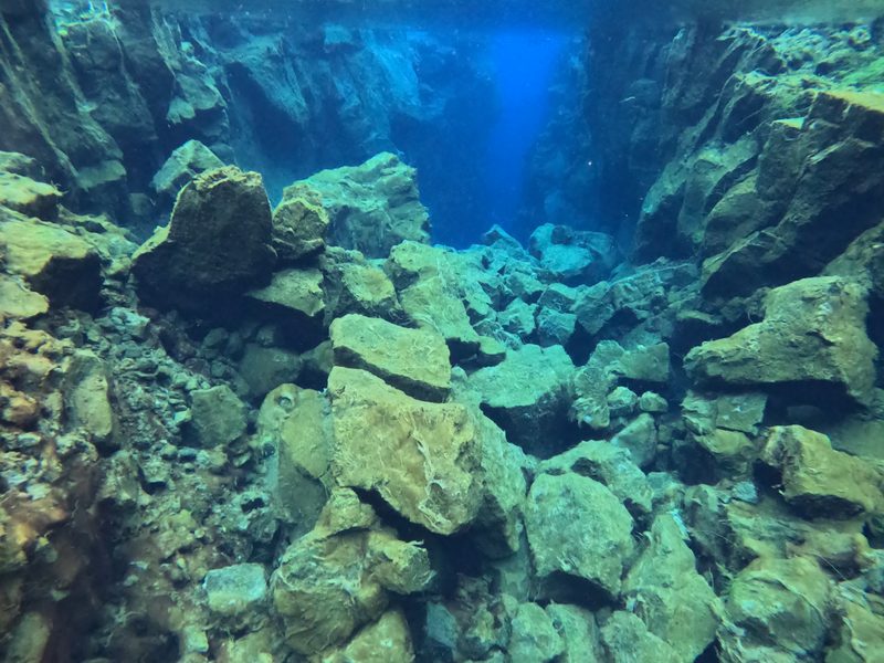 Jagged lava rock formations lining the narrow Silfra fissure underwater
