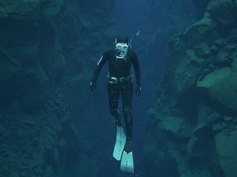 A freediver descending through the narrow Silfra fissure in freedive fins