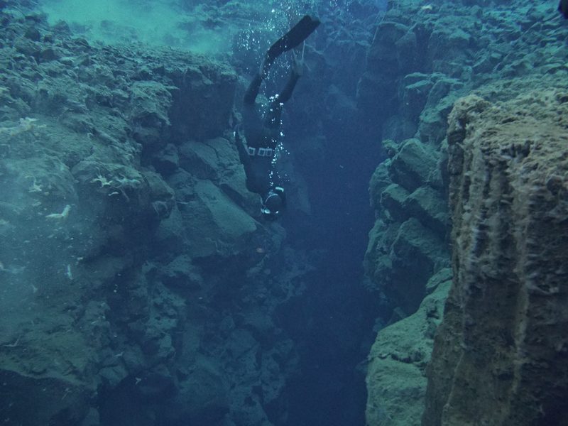 A freediver descending between steep rock walls in the Silfra fissure