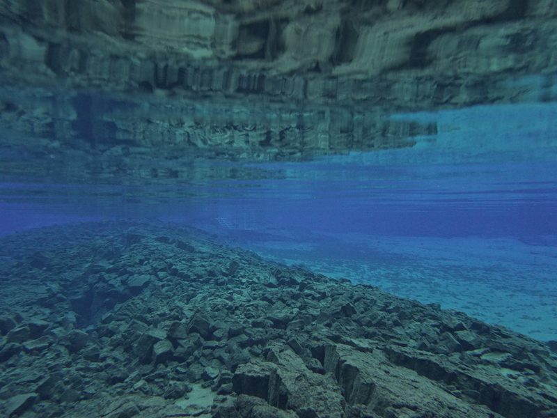 Underwater view of a rocky ridge beneath the glassy surface of the fissure