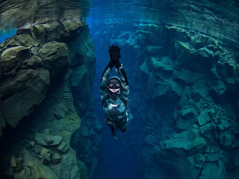 A freediver ascending with arms raised between two rock walls in Silfra