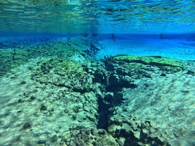 Snorkelers at the surface above a narrow rock fissure splitting the seabed