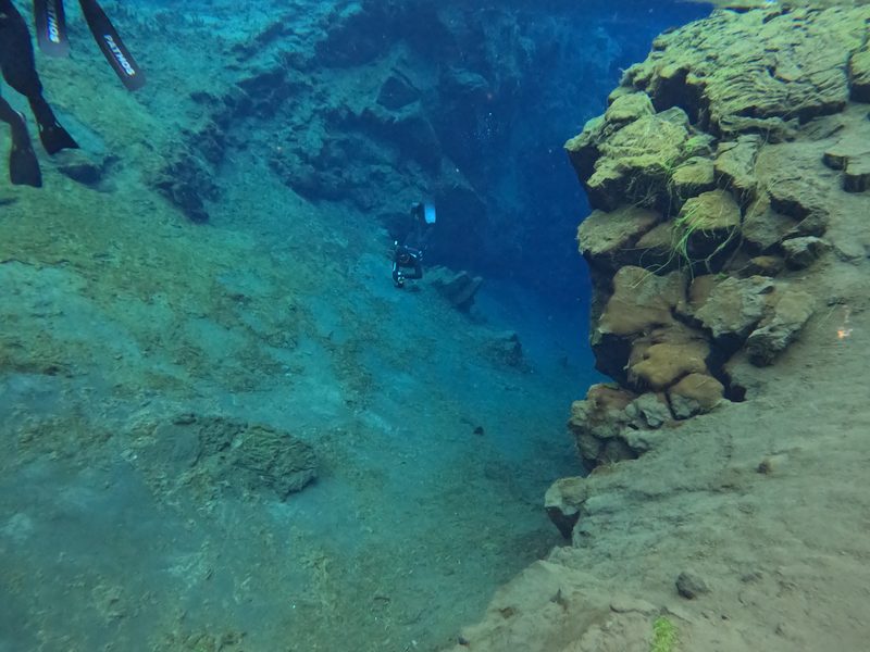 A freediver exploring a mossy underwater ledge in the Silfra fissure