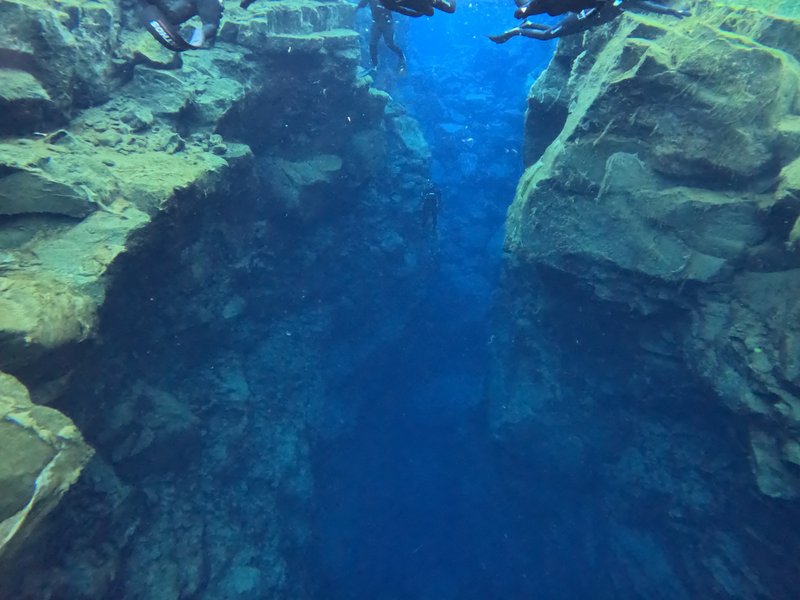 Freedivers descending into the deep blue channel of the Silfra fissure